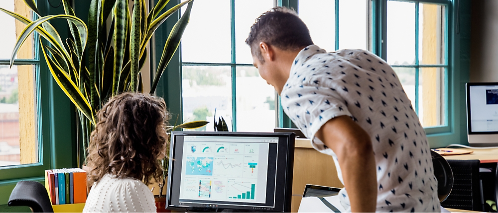 Two people in an office analyze data displayed on a computer screen.