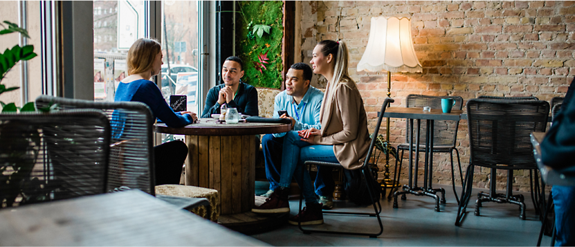 Four people sitting at a round table in a cozy cafe, engaged in conversation.