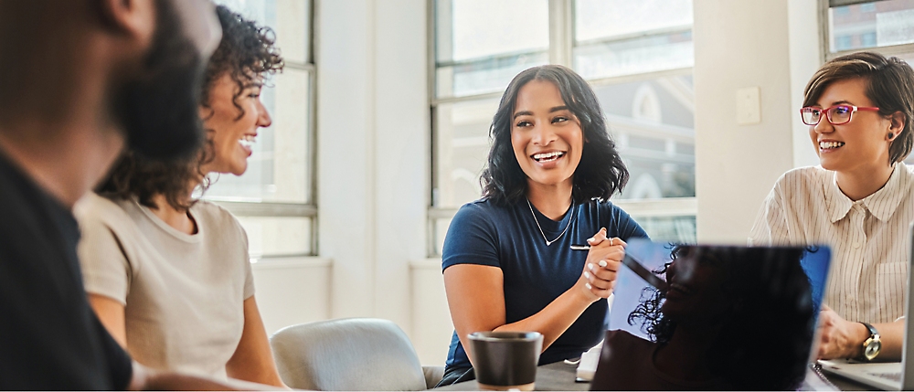 Four people sit around a table engaged in a lively conversation, with two women in focus, smiling and interacting.