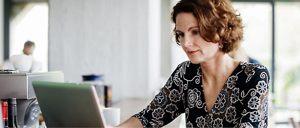 A woman with short curly hair uses a laptop at a counter in a well-lit room.