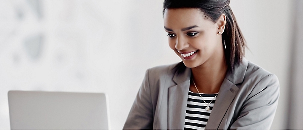 A woman in a gray blazer and striped shirt is smiling while looking at a laptop.