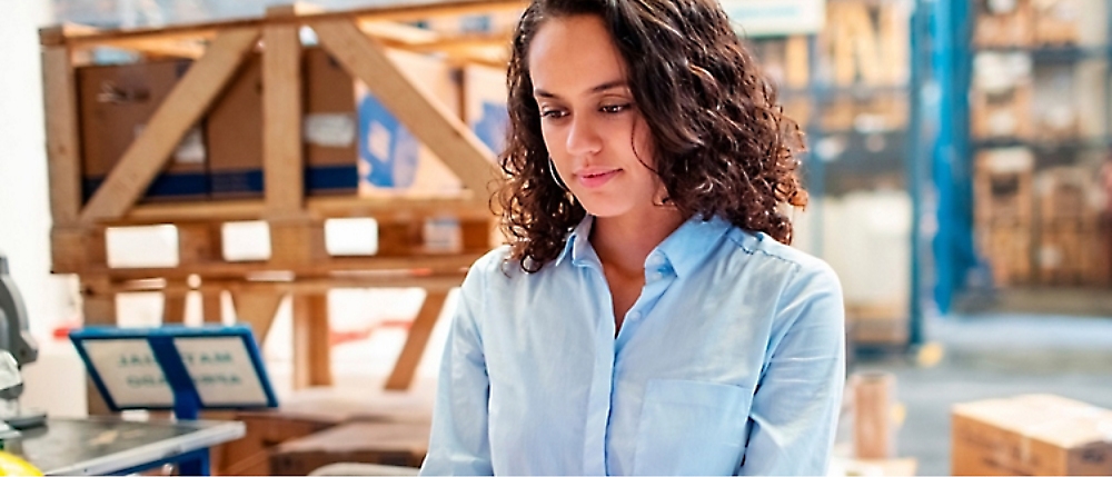 Person with curly hair and a light blue shirt is standing in a warehouse 