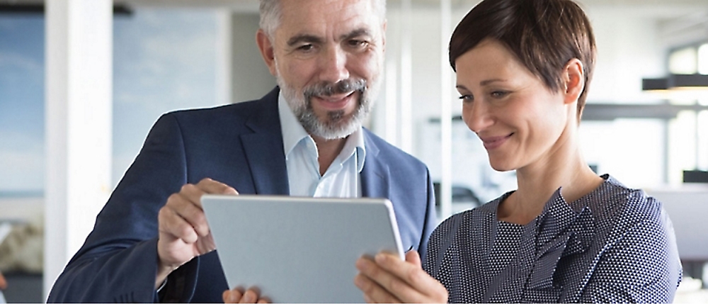 Two people in an office setting looking at a tablet. 