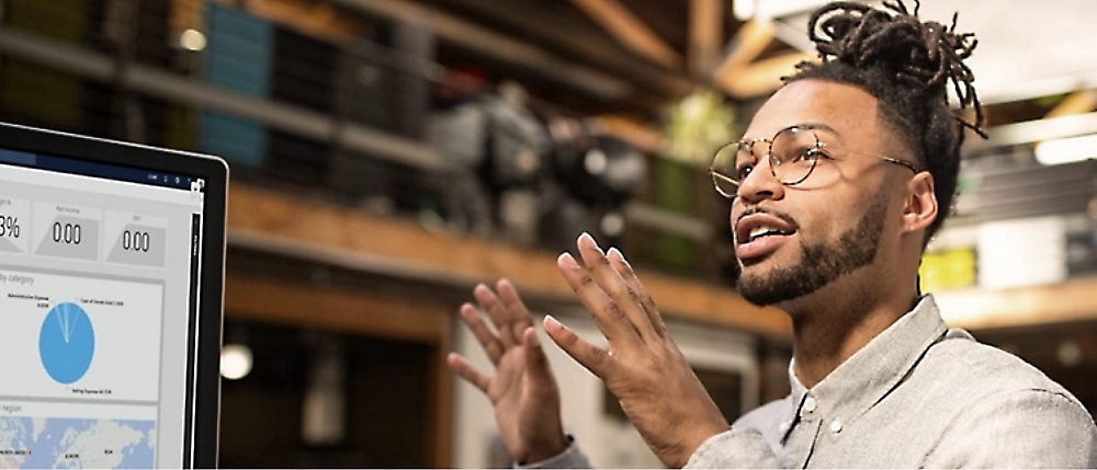 A person with glasses is explaining data displayed on a computer screen showing charts 