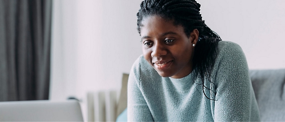 A person with braided hair and a green sweater is looking at a screen with a slight smile.