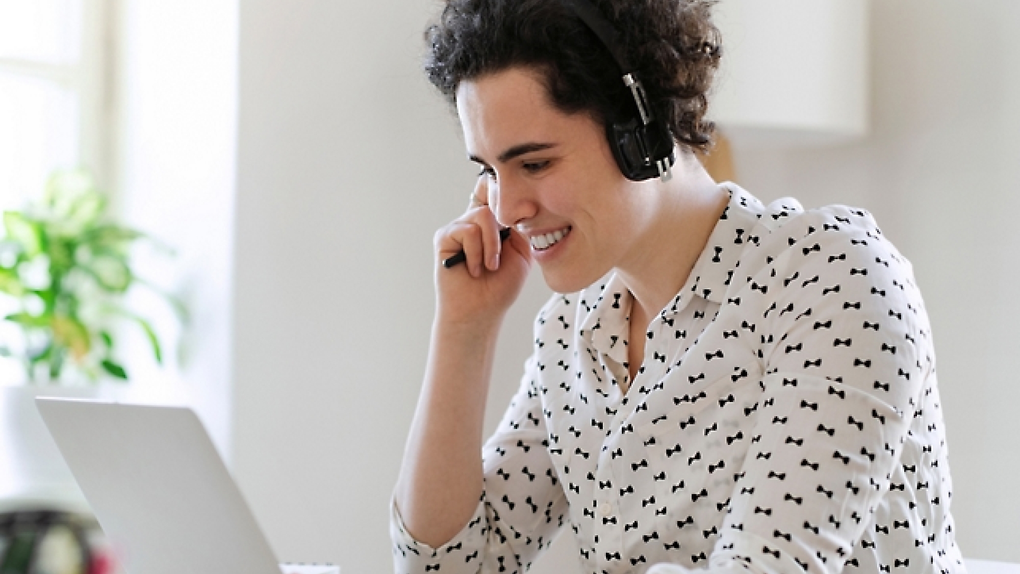 Person with curly hair wearing headphones and a white shirt with black bowtie patterns