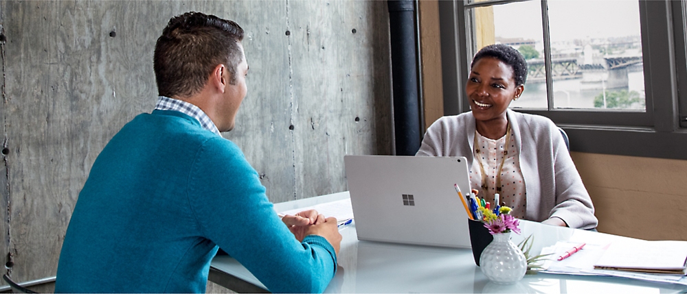 Two people are seated across from each other at a desk, engaged in a conversation.