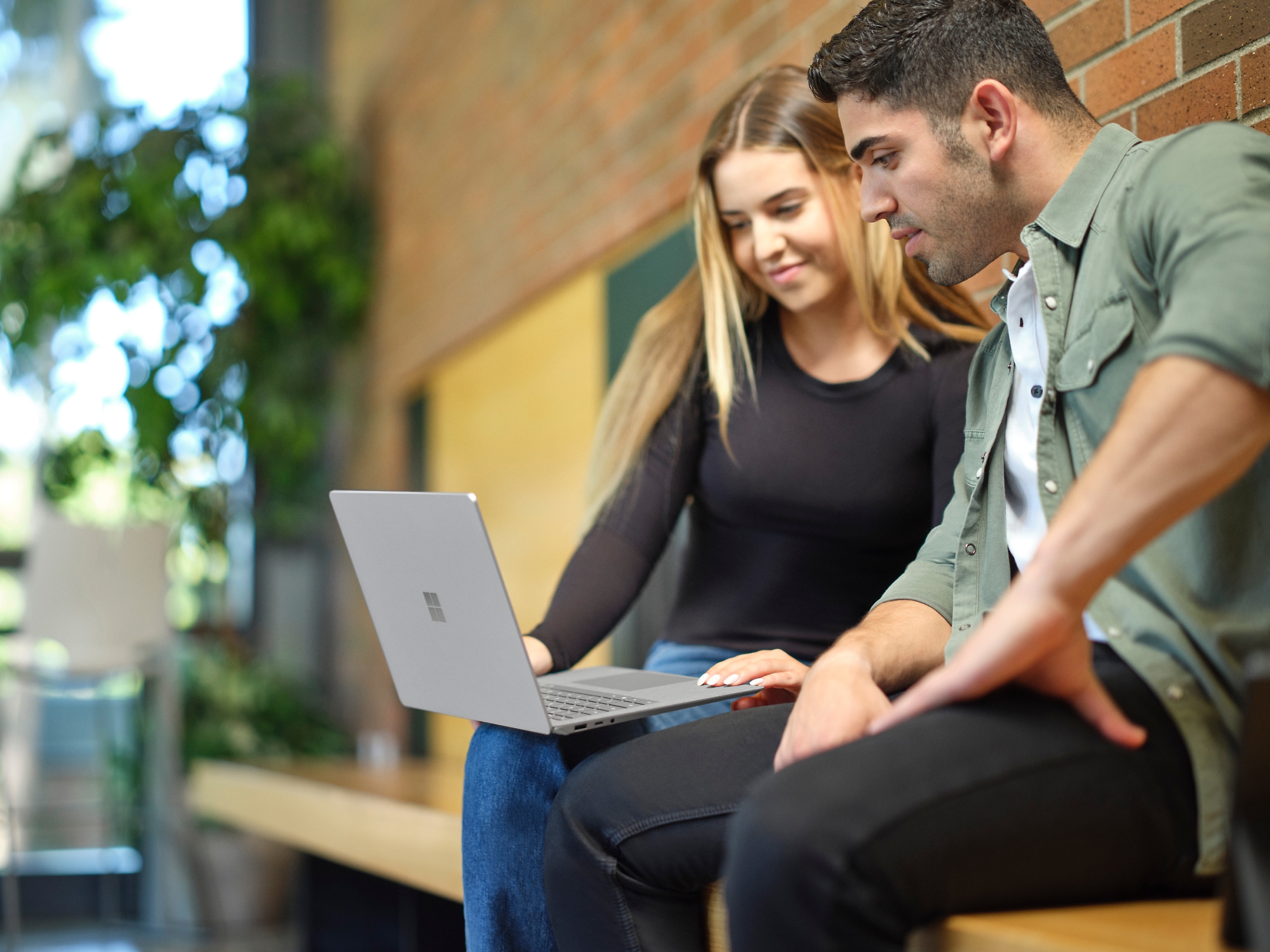 A person and another person sitting on a bench looking at a computer.