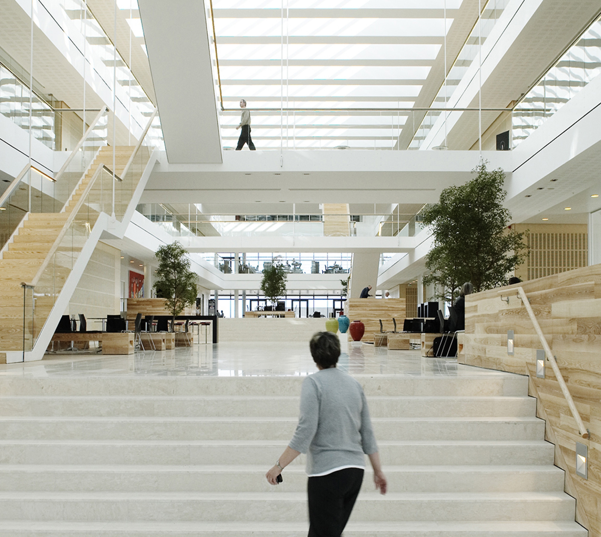 Moderne kontorlobby med store hvite trapper, treuthevinger og personer som går rundt. Lys og luftig atmosfære.