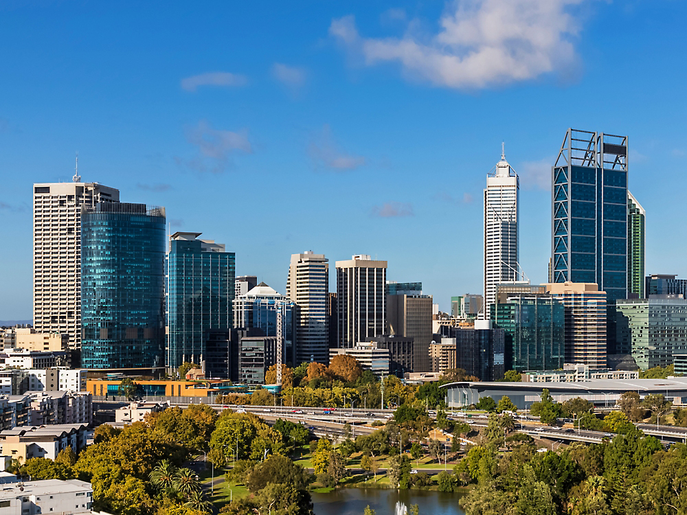 En horisont av Perth, Australia, viser moderne høyhus mot en klar blå himmel, med frodig grøntområde i forgrunnen.