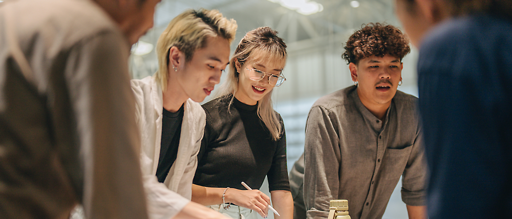 A group of people standing and discussing, looking over a desk