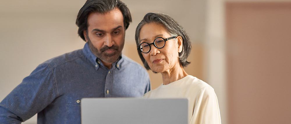 A middle-aged man and an elderly woman looking at a laptop screen together, possibly discussing its content.