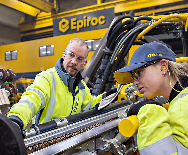 To teknikere iført refleksvest arbejder på industrimaskiner i en Epiroc-facilitet.