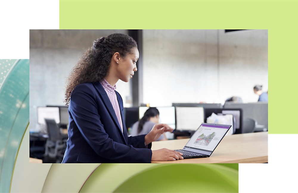 A woman with curly hair working on a laptop in a modern office environment.