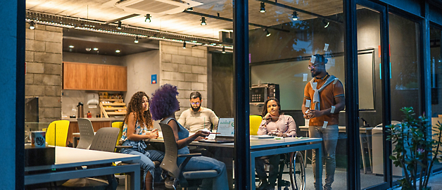 Four individuals in a modern office space during an evening meeting, with one person presenting.