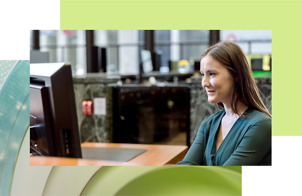 صورة لامرأة ترتدي سترة خضراء تبتسم خلال استخدام الكمبيوتر في أحد المكاتب.