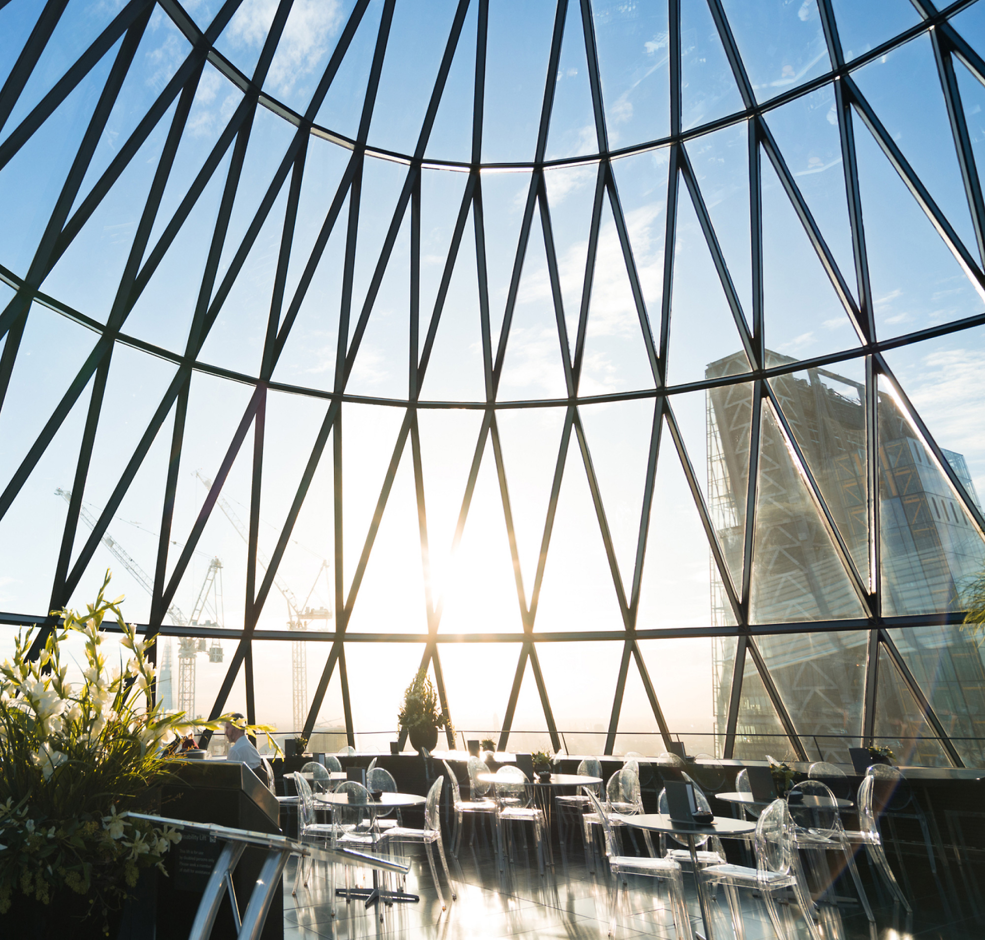 La lumière du soleil s’insère dans un grand coupole de verre géométrique qui donne sur une ville et qui éclaire une salle à manger intérieure 