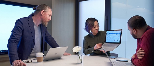 Three professionals discussing over a laptop in a modern office setting.