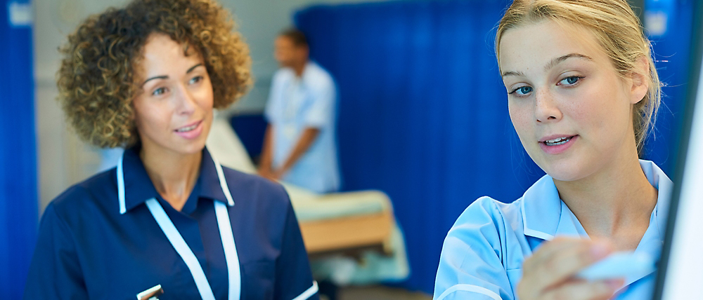 صورة لامرأتان متخصصتان في الرعاية الصحية في مستشفى، إحداهما تشير وتشرح شيئًا ما، مع عضو آخر بفريق العمل 