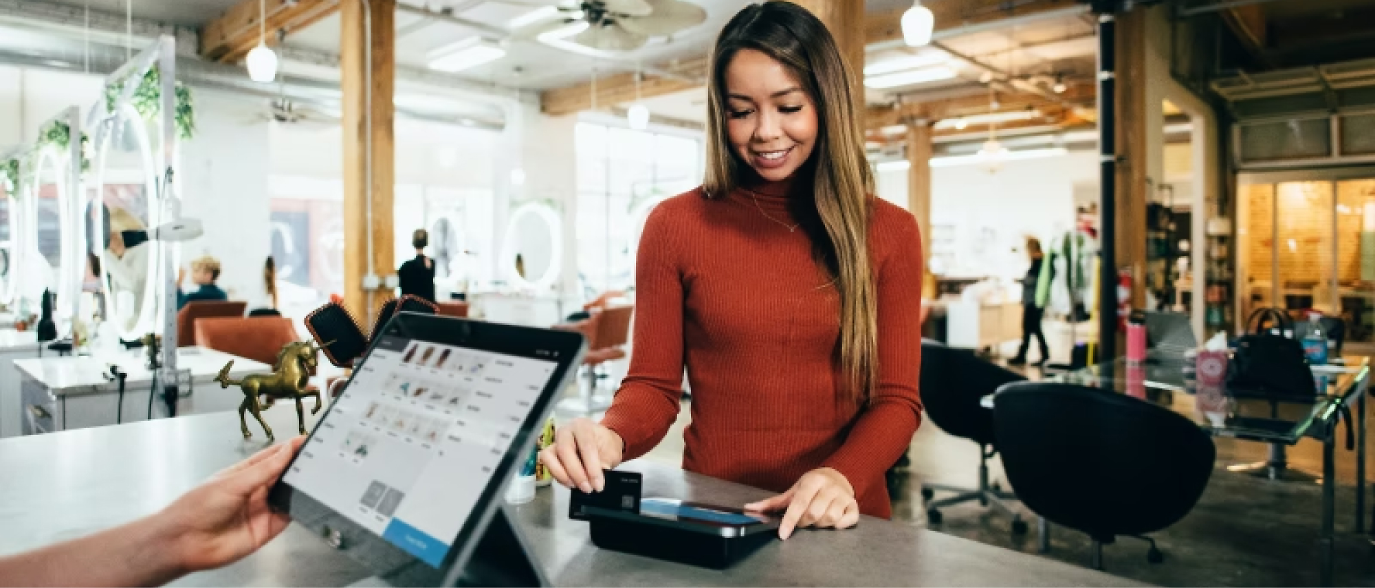 A woman uses a card to make a payment at a touchscreen terminal in a modern, open-concept store.