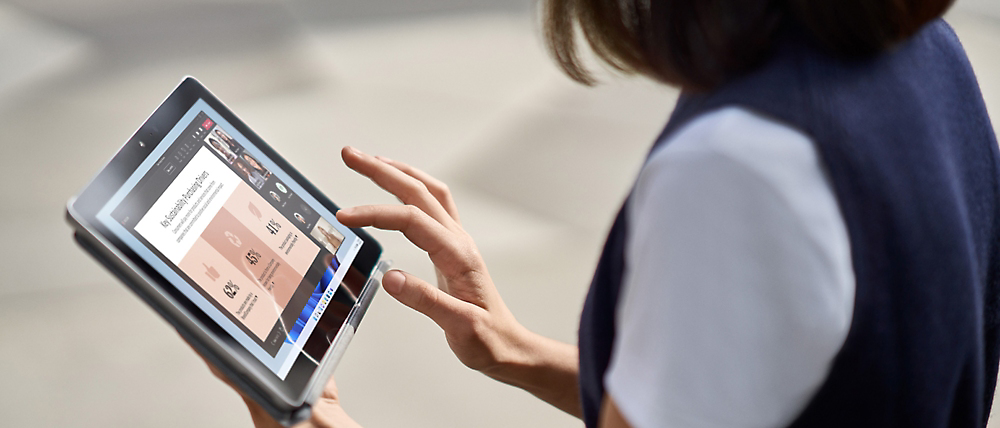 A person using a tablet with a sports app open, interacting with the touchscreen while standing outdoors.