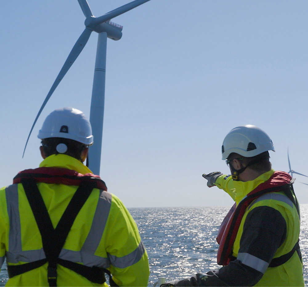 A couple of men in safety gear pointing at wind turbines