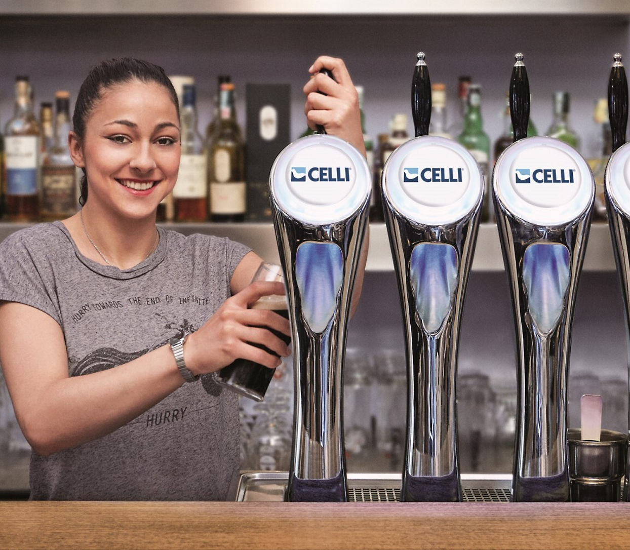 A bartender fills a glass from a draft beer dispenser in a bar, with bottles of liquor 