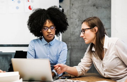 Two people in a conference room talk in front of a laptop.