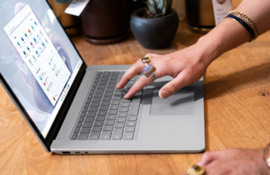 An adult working on a Surface Laptop 5 which is sitting on a desk along with several plants.