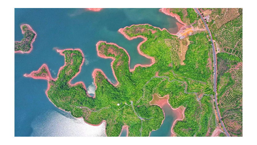 Aerial view of land with greenery and roads jetting out into a large body of water.