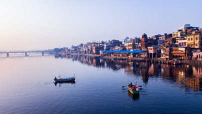 Two small boats on a lake in front of a city, with a bridge in the distance.