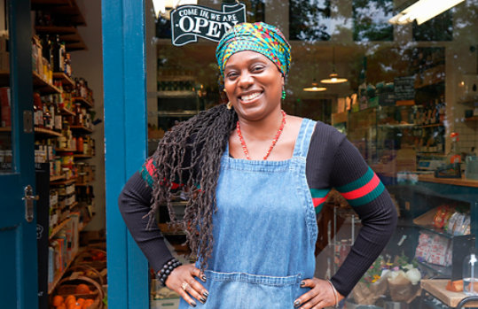 A smiling woman standing outside the entrance of her shop.