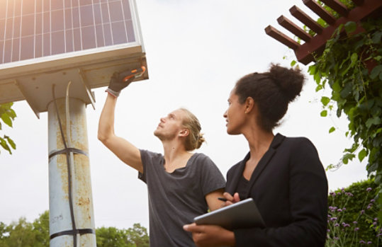 Low angle view of a garden architect adjusting a solar panel with a colleague holding a tablet computer.