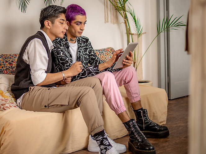 Two persons are sitting on a sofa and looking into the tablet