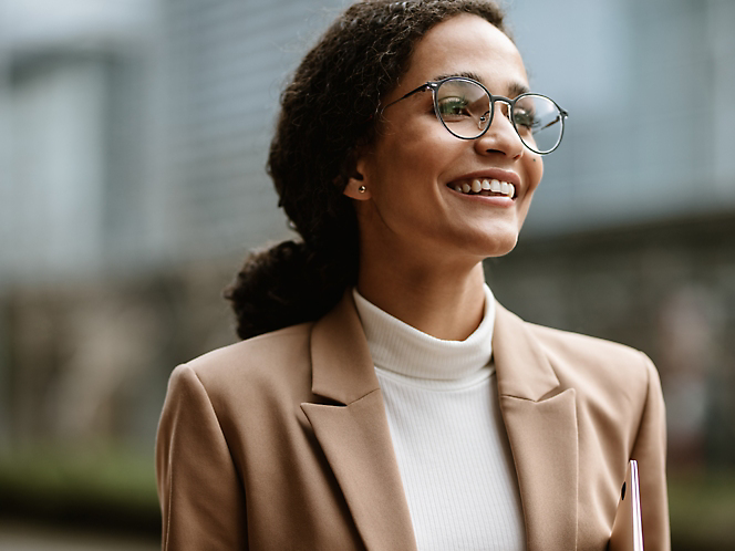 A woman wearing glasses and a blazer is smiling.