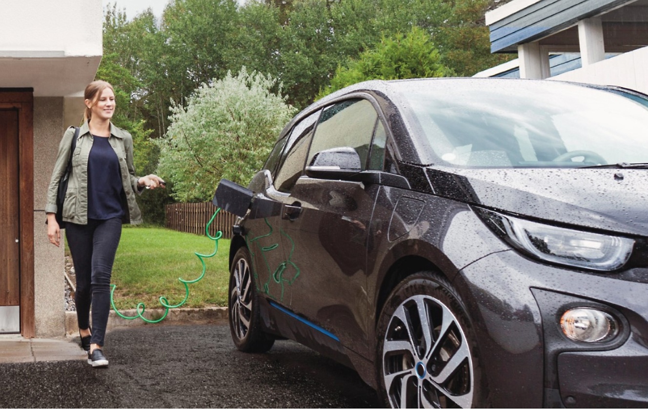 Uma mulher está carregando seu BMW i3 na frente de uma casa.