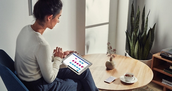 A person sitting at a small round table with a cup of coffee using a tablet device to create a chart.