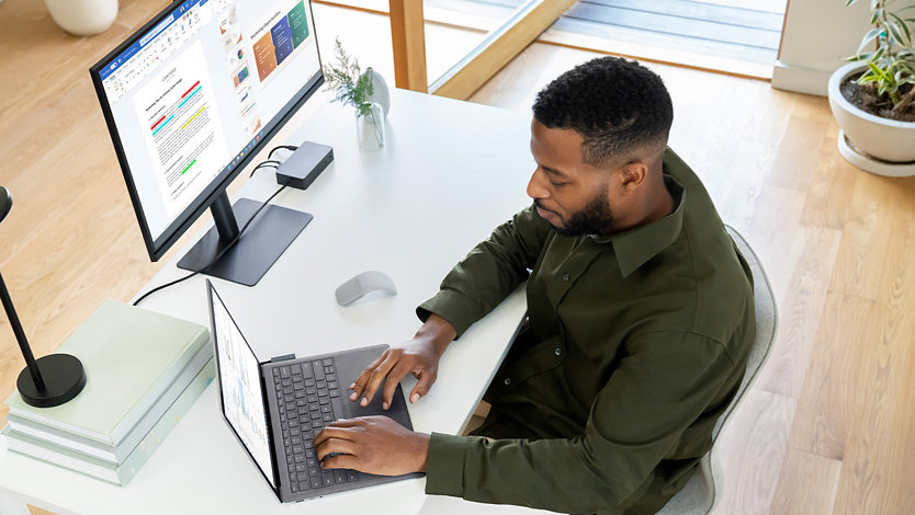 Una persona, sentada en un escritorio en una oficina, usa Surface Laptop 5 para empresas. 