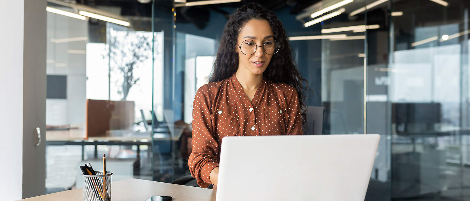 A girl is sitting at a desk, working with a laptop.