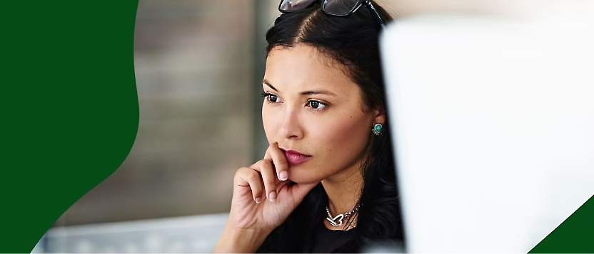 A woman focusing on her computer screen, hand on chin, wearing glasses on her head and turquoise earrings