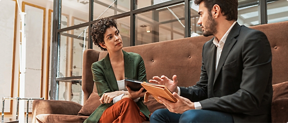 Two persons sitting, holding tablets and discussing on some topic.