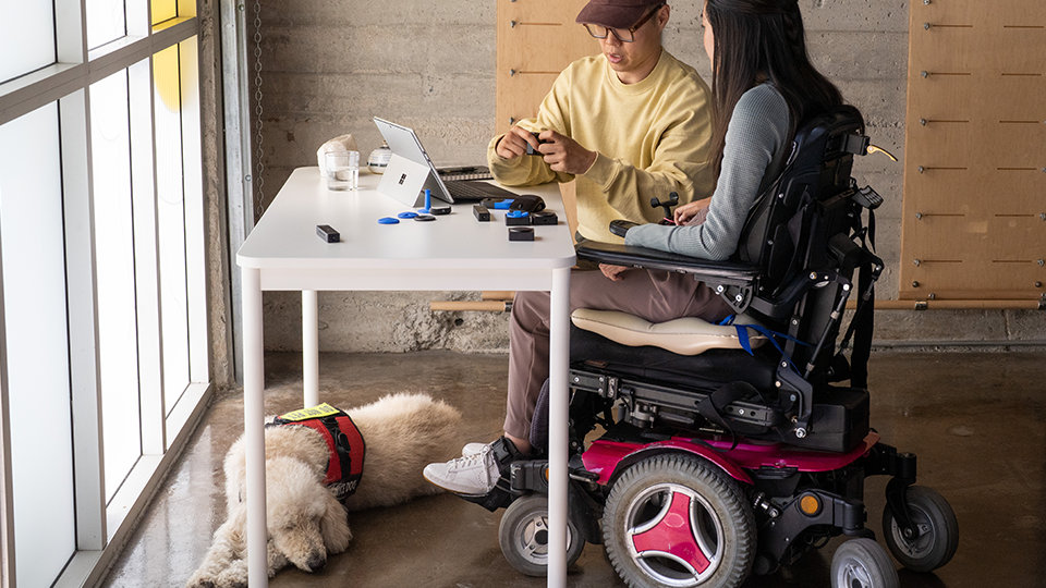 A person who uses a wheelchair tests Microsoft adaptive accessories with a coworker.