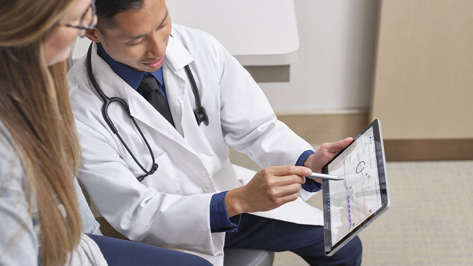 Un médico usa un Lápiz para Surface para empresas para interactuar con la pantalla táctil de un dispositivo Surface Go 4 para empresas mientras habla con un paciente.