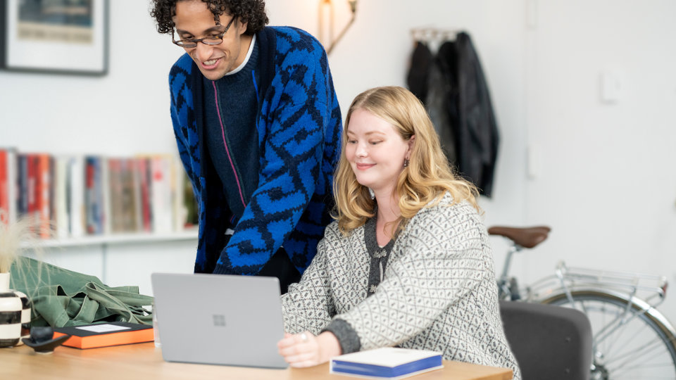 Iemand toont het scherm van zijn Surface Laptop Go 3 voor zakelijk gebruik aan een andere persoon waarmee wordt verduidelijkt dat de beveiligde kern de nodige bescherming heeft geboden om zijn gevoelige gegevens te vergrendelen.