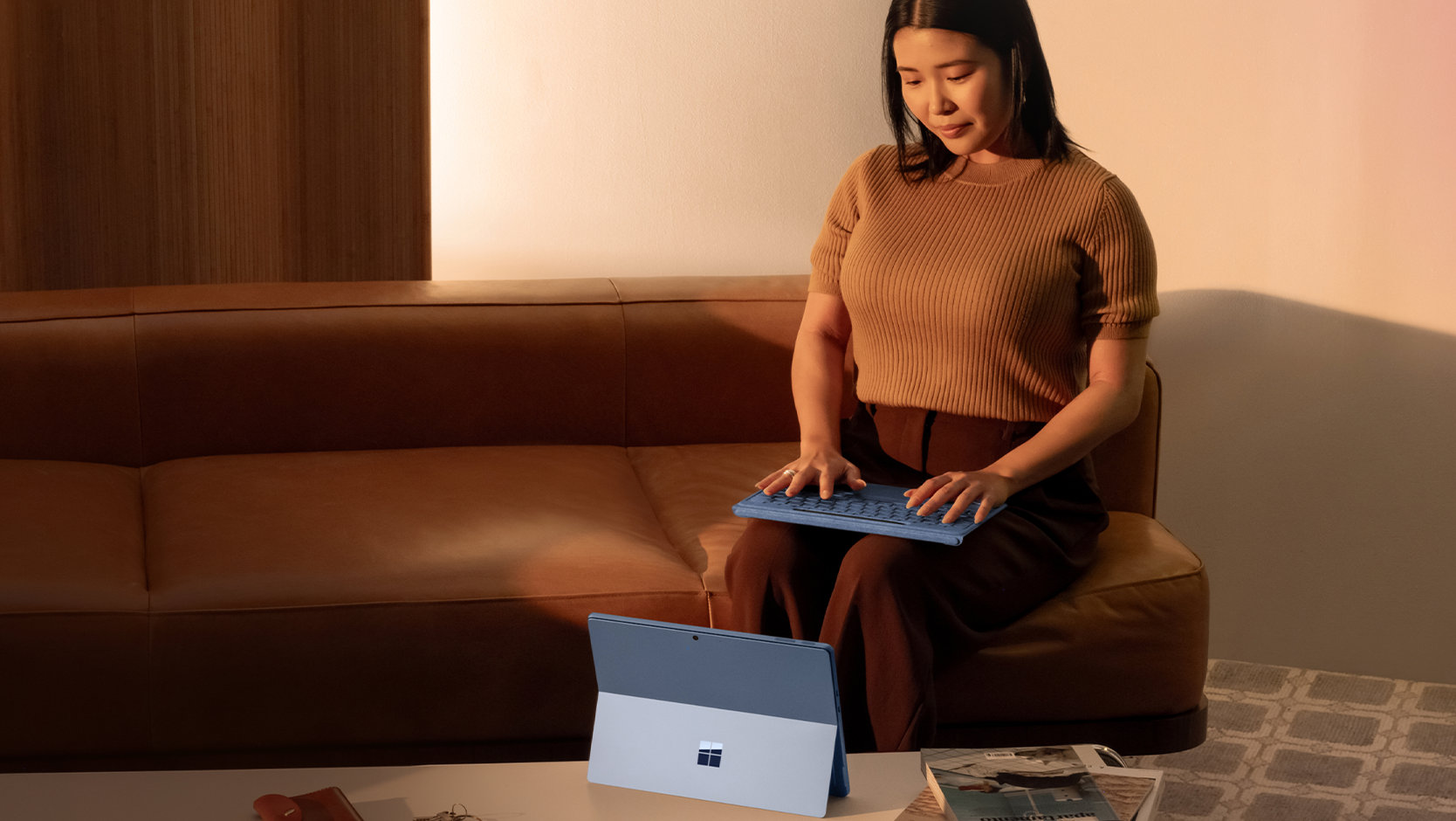 A person uses a detached Surface Pro Flex Keyboard with Slim Pen in their lap to type on a Surface device that’s set up on a table. 