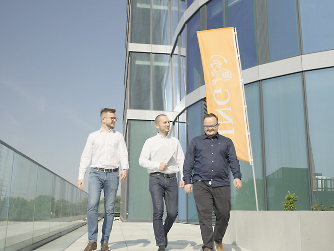 Tres hombres saliendo de un edificio con una bandera naranja de ING de fondo 