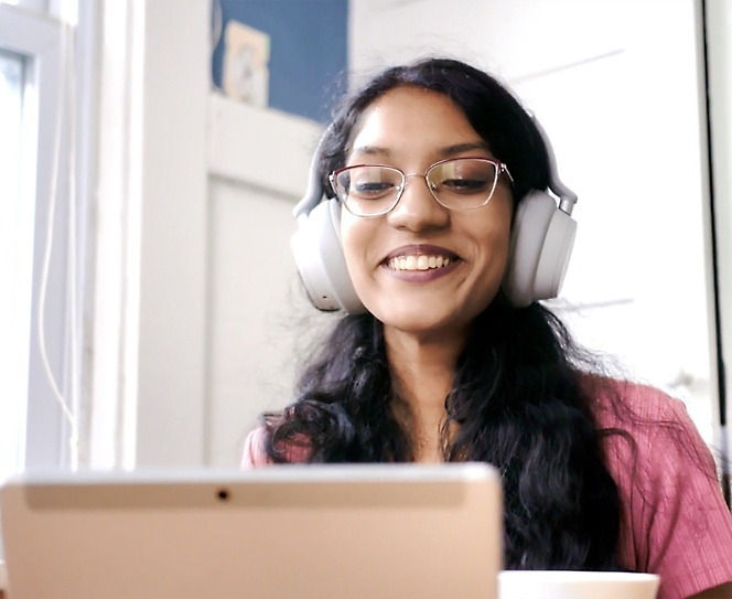 A woman with spectacles and headphones smiling and using her laptop