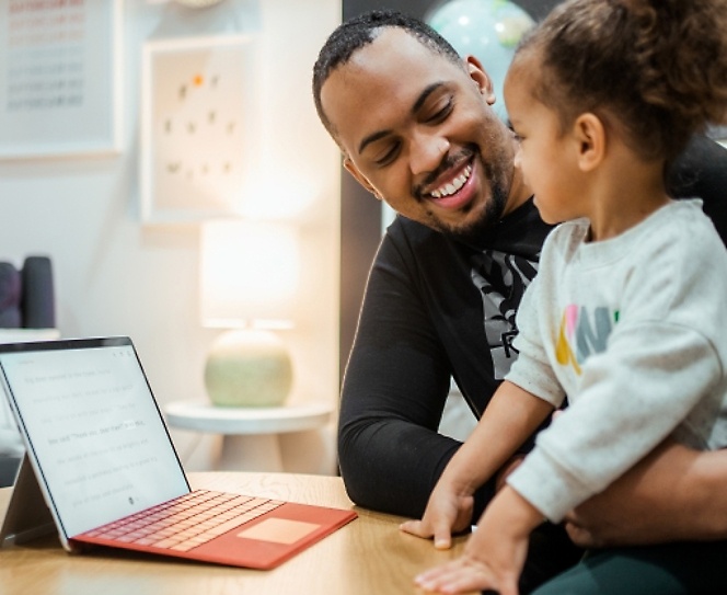 A person smiling looking at the kid along with a laptop placed on the table