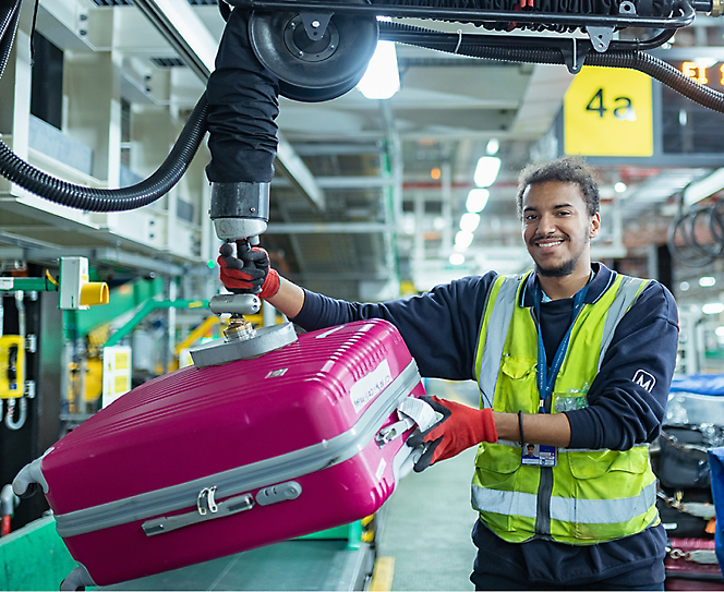 A worker in safety jacket handling pink suitcase