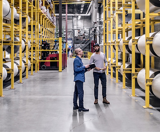 Two people in a warehouse talking to each other.